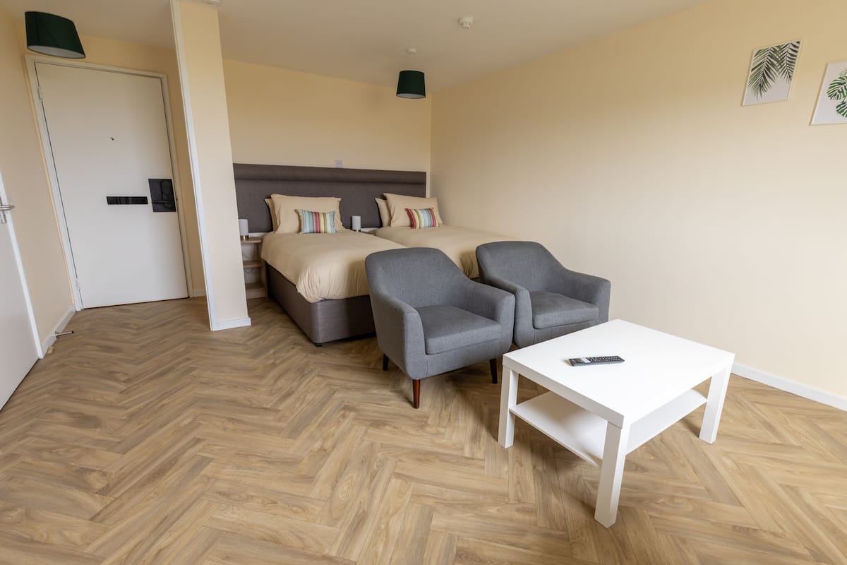 A hotel room with a bed, two armchairs, a white coffee table, and a door.