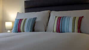 A bed with two pillows, a nightstand with a lamp, and a dark headboard. - Wick Bay Apartments (Wick)