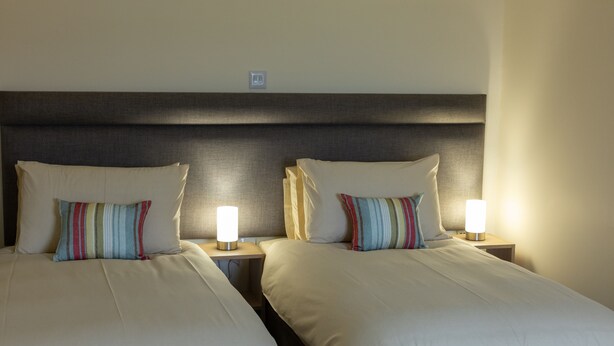 Two single beds with striped pillows and bedside lamps in a hotel room. - Wick Bay Apartments (Wick)