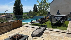 Patio esterno con piscina, poltrona prendisole, tavolo e un braciere.