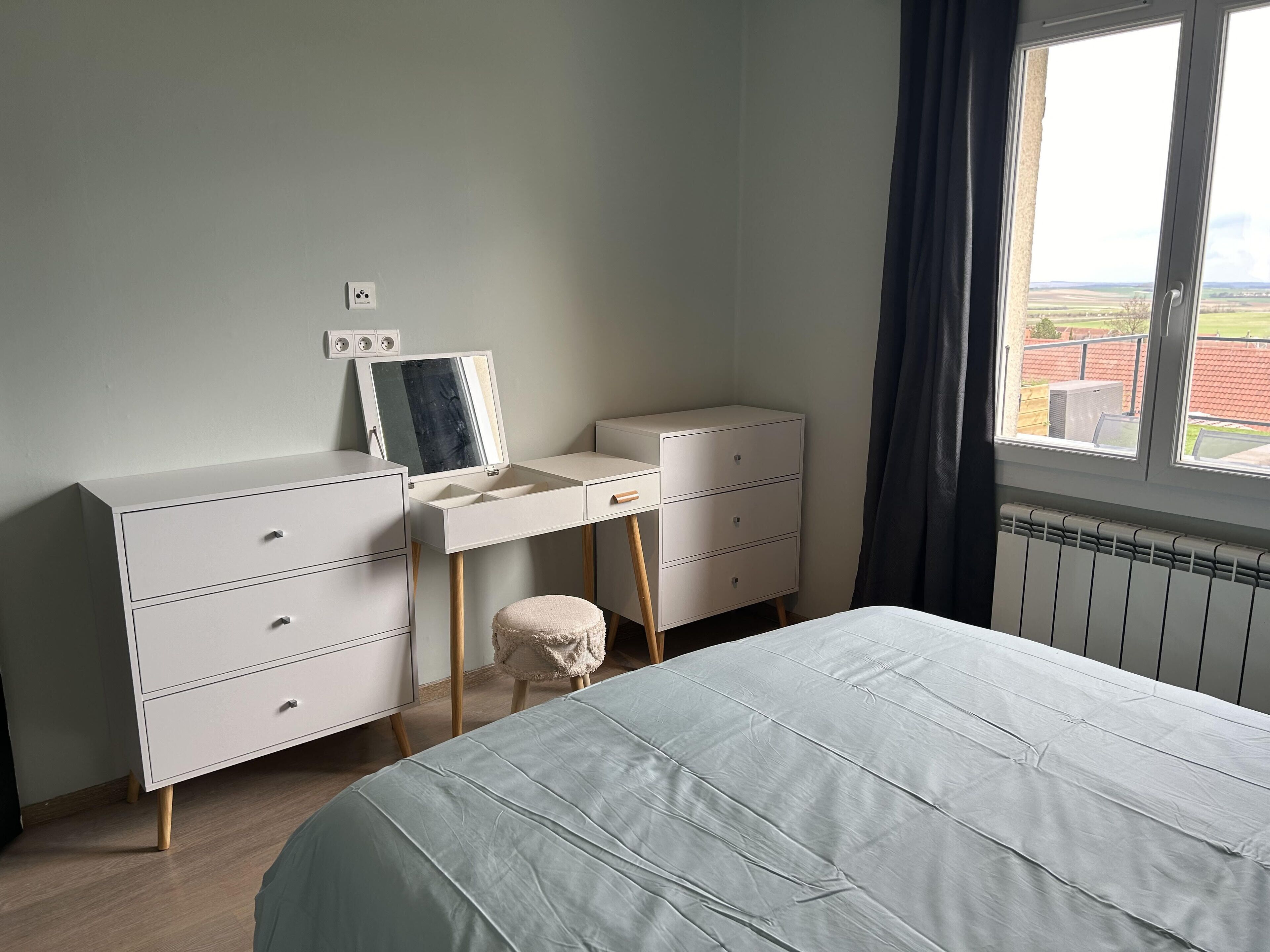 A bedroom with a bed, a dresser with drawers, a mirror, and a window with a view of the outdoors.