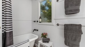 Une salle de bain avec une baignoire, une fenêtre donnant sur un beau paysage, un porte-serviettes et une petite table sur laquelle sont posés une serviette et des fleurs.