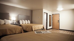 A hotel room with two beds, a nightstand, a lamp, and a door. - The Lodge at Moorcroft (Moorcroft)