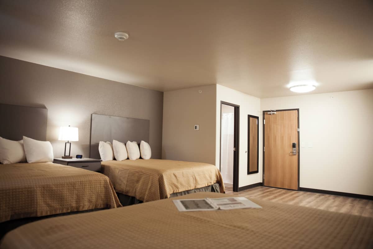 A hotel room with two beds, a nightstand, a lamp, and a door.