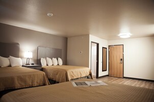 A hotel room with two beds, a nightstand, a lamp, and a door.
