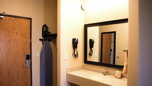 A hotel bathroom with a wooden door, a mirror, a sink, and a hairdryer on a wall-mounted rack. - The Lodge at Moorcroft (Moorcroft)