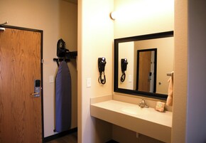 A hotel bathroom with a wooden door, a mirror, a sink, and a hairdryer on a wall-mounted rack.