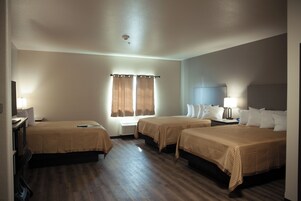 A hotel room with two beds, a desk, a chair, a window with curtains, and a ceiling light.