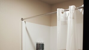 A shower with a white curtain, a shelf with toiletries, and a towel on the floor. - The Lodge at Moorcroft (Moorcroft)
