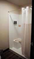 A shower with a white curtain, a shelf with toiletries, and a towel on the floor.