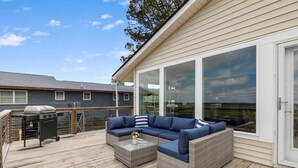 A covered outdoor patio with a wicker sofa, a glass-top coffee table, and a barbecue grill.