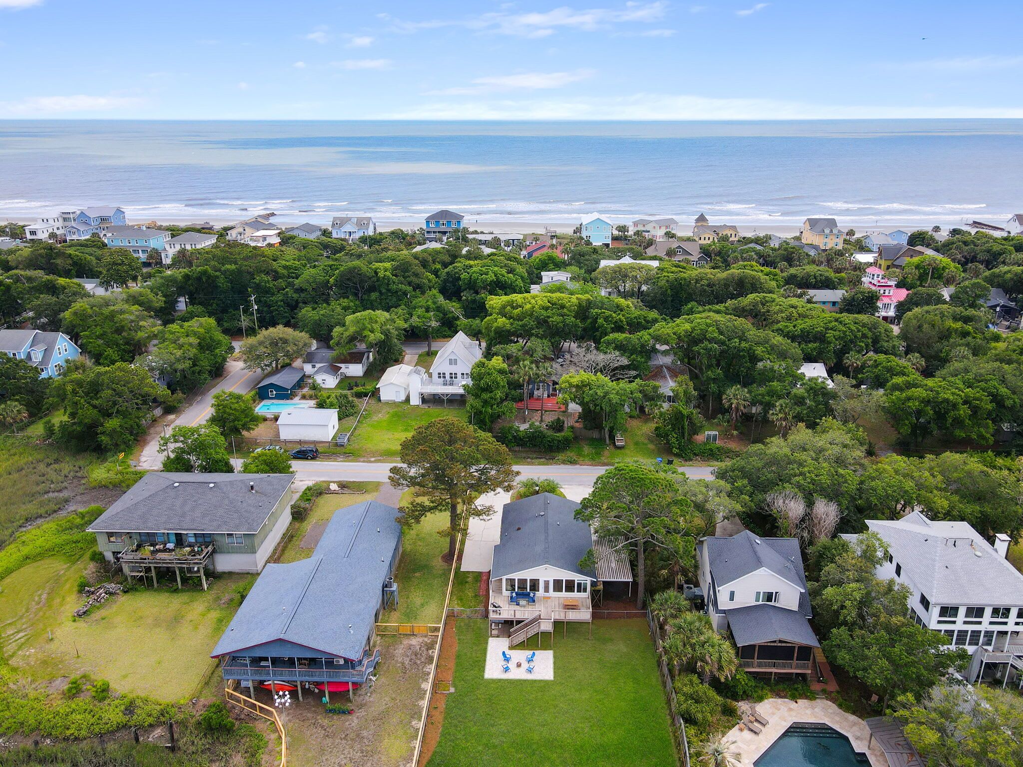 An aerial view of a coastal residential area with houses, a swimming pool, and a view of the ocean.