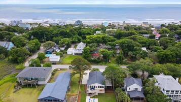An aerial view of a coastal residential area with houses, a swimming pool, and a view of the ocean.