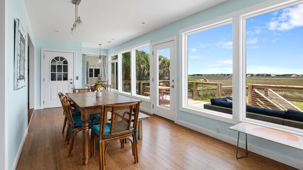 A spacious dining area with a wooden table and chairs, large windows offering a view of the outdoors, and a door leading to another room.