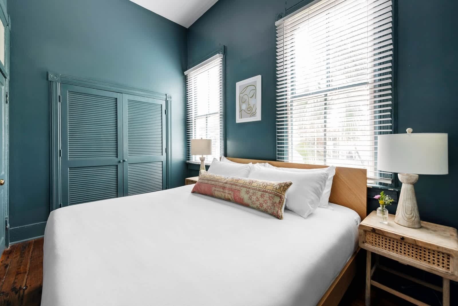 A bedroom with a large bed, two bedside tables, a nightstand, and a window with blinds.