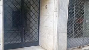 A closed metal gate with a diamond pattern, a number '17' on the wall, and a chain-link fence to the right. - pnoe d'Athènes (Athina)