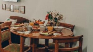 A dining area with a round wooden table, six chairs, and various paintings on the wall. - pnoe d'Athènes (Athina)