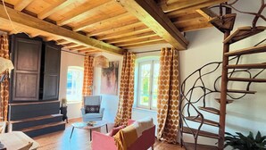 A rustic interior with exposed wooden beams, a pink sofa, a wooden ladder, and a chair with a patterned cushion.