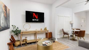 A modern living room with a flat-screen TV mounted on the wall, a wooden console table, a round coffee table, and a grey sofa.