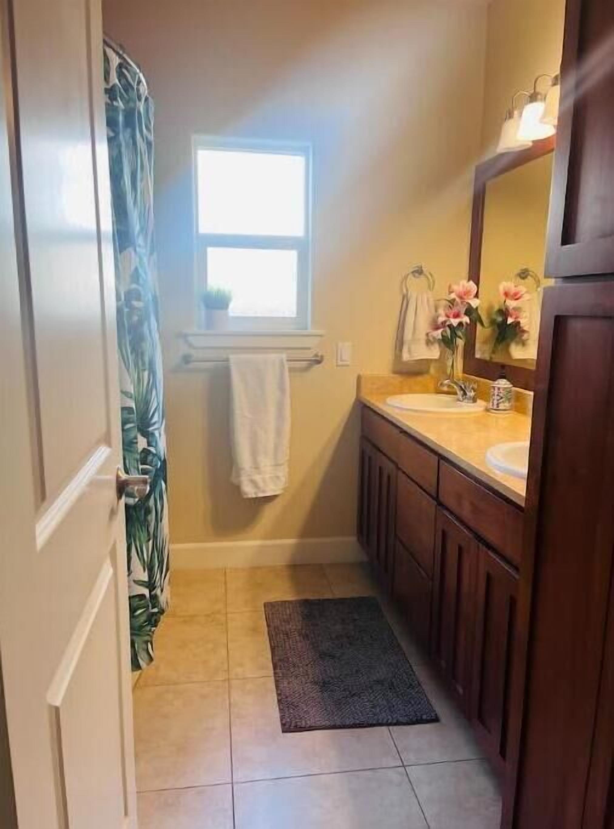 Une salle de bain avec un rideau de douche, une fenêtre, un lavabo, un miroir et un porte-serviettes.