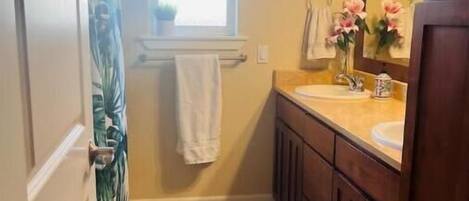 A bathroom with a shower curtain, a window, a sink, a mirror, and a towel rack.