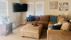 Una sala de estar con un sofá color beige, una mesa de centro y un televisor de pantalla plana montado en la pared.