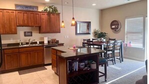 Una cocina moderna con armarios de madera, una zona de comedor con mesa y sillas, y una pequeña isla con espacio para vinos.