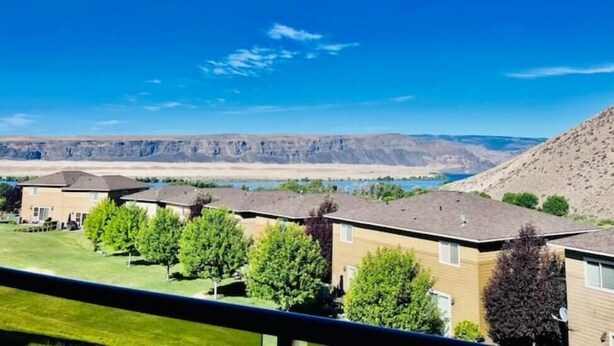 Zona residencial con varias casas, cielo azul despejado y una vista distante de un cañón.
