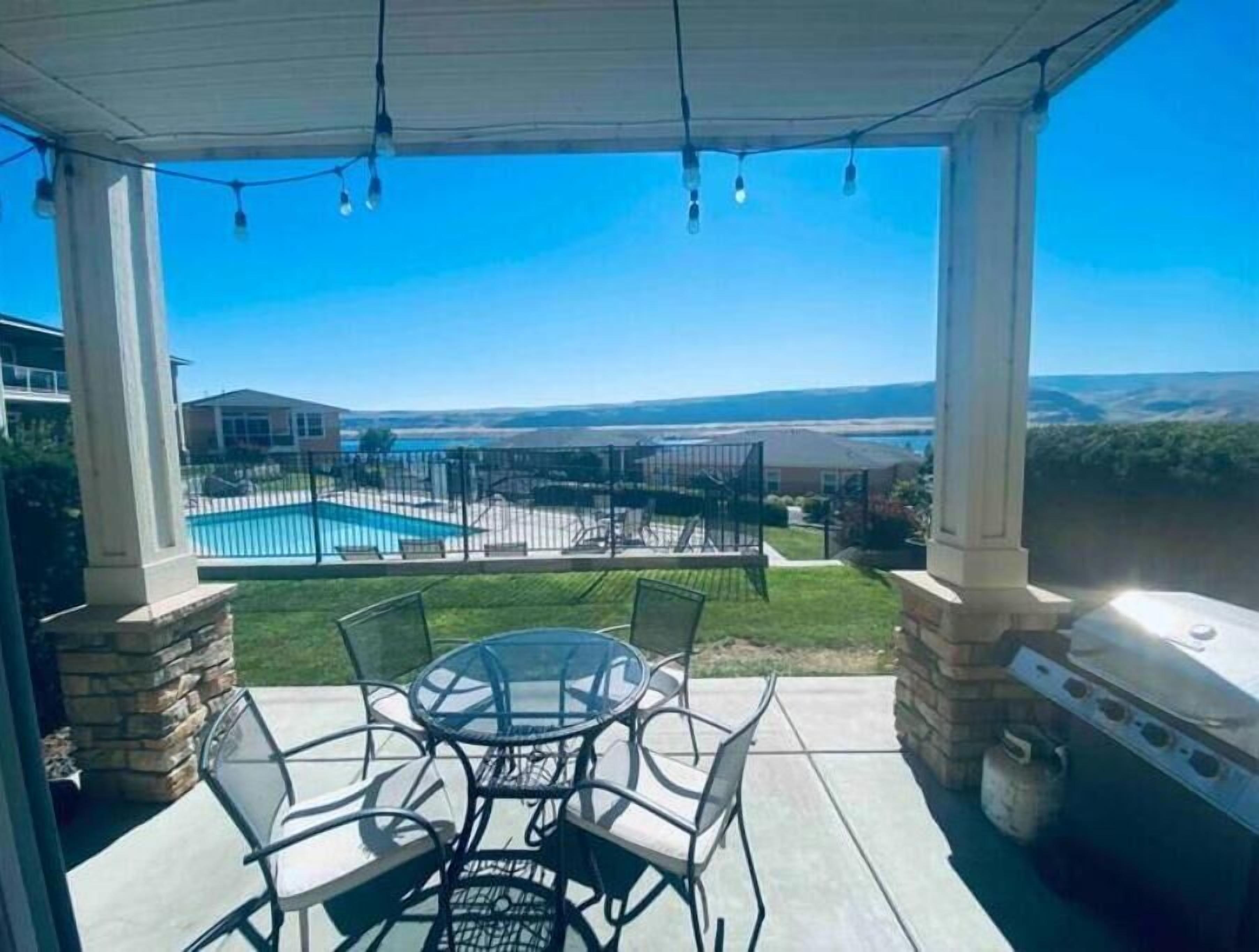 Eine überdachte Terrasse mit Glastisch und -stühlen, mit Blick auf ein Schwimmbad und einen umzäunten Garten.