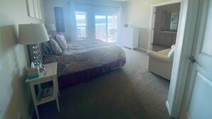 Ein Schlafzimmer mit einem Bett, einem Nachttisch, einem Sessel, einem Deckenventilator und Blick ins Freie durch ein Fenster.