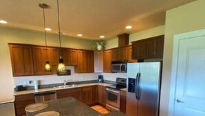 A modern kitchen with granite countertops, wooden cabinets, stainless steel appliances, and pendant lighting. - A28 condo by large pool/shuttle (Quincy)