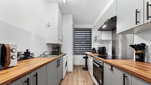 A modern kitchen with wooden countertops, stainless steel appliances, and grey cabinetry. - Elegant 1 Bdr Flat in Goodmayes w Free Parking (Ilford)