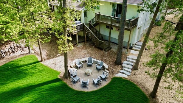A circular outdoor seating area with chairs and a fire pit, surrounded by trees and a building with a balcony. - Downtown Sister Bay | Arcade, Deck, Fire Pit (Sister Bay)
