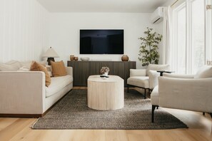 Un salon moderne comprenant un canapé, un fauteuil, une table basse et un téléviseur à écran plat fixé au mur.
