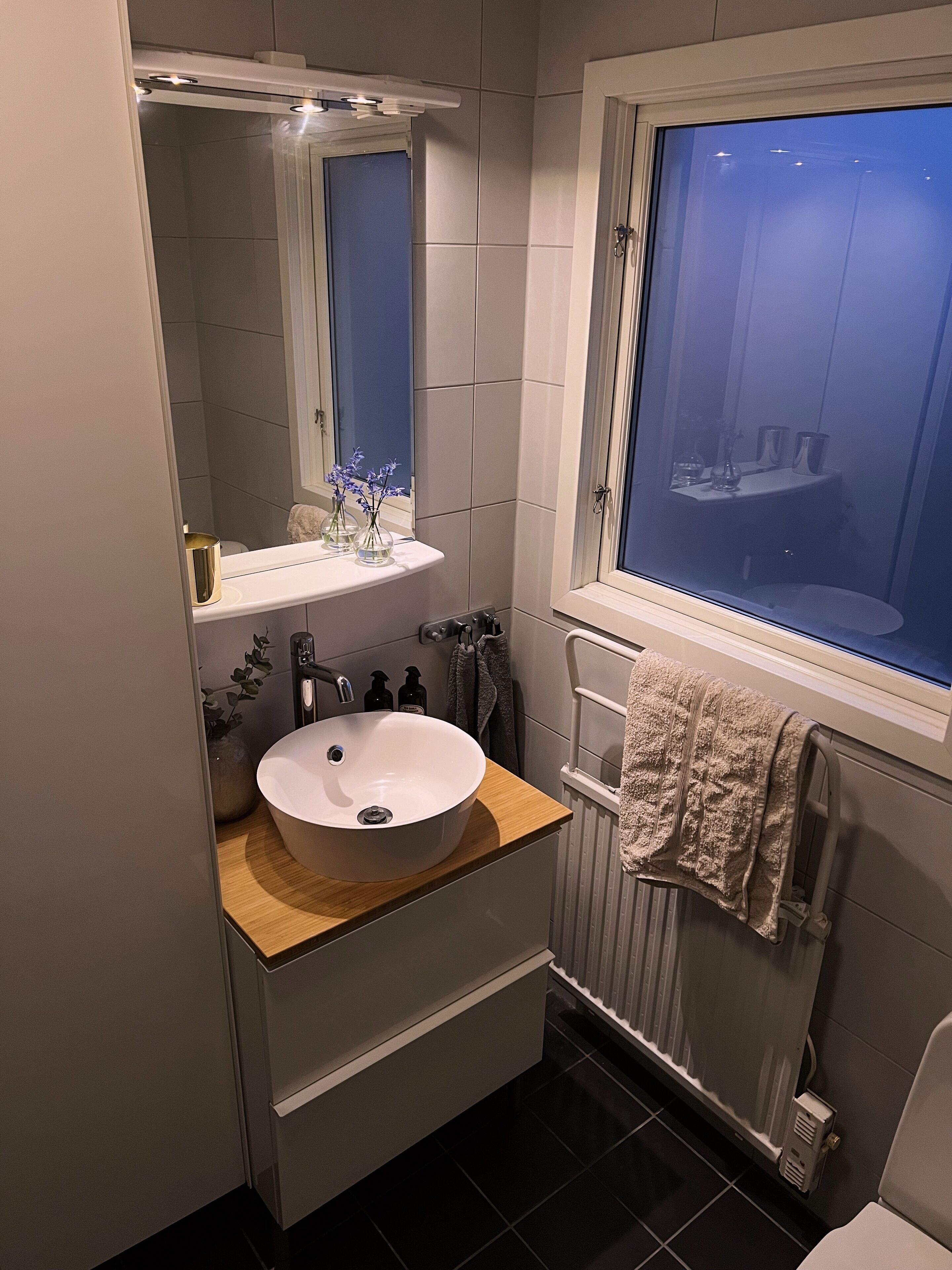Une salle de bain avec un lavabo blanc, un miroir, une fenêtre et un porte-serviettes.