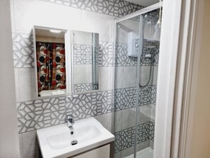 A bathroom with a white sink, a glass shower enclosure, and patterned tiles.