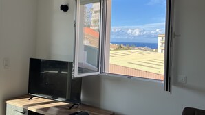 Ein Zimmer mit großem Fenster, einem Fernseher auf einem Holzboden und einer Wandleuchte.