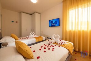 Habitación de hotel con dos camas, cada una con sábanas blancas y almohadas amarillas, y un televisor que muestra el logotipo de Disney Channel.