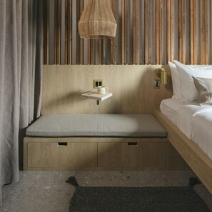 Ein modernes Schlafzimmer mit einer eingebauten Sitzbank, einem kleinen Regal mit Buch und Tasse, einer Hängeleuchte und einem Bett mit weißer Bettwäsche.