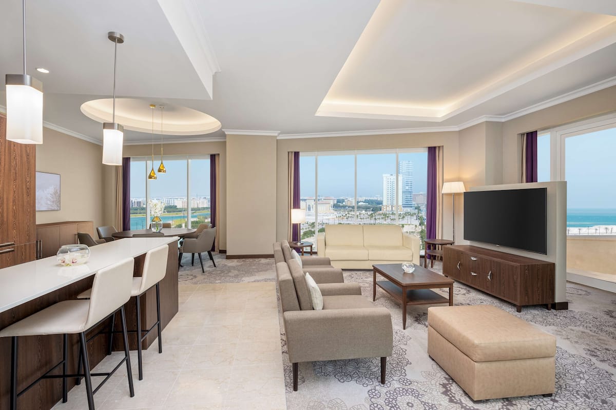 Quarto de hotel moderno com área de refeições, assentos, televisão e vista para a cidade.