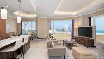 A modern hotel room with a dining area, seating, a TV, and a city view.