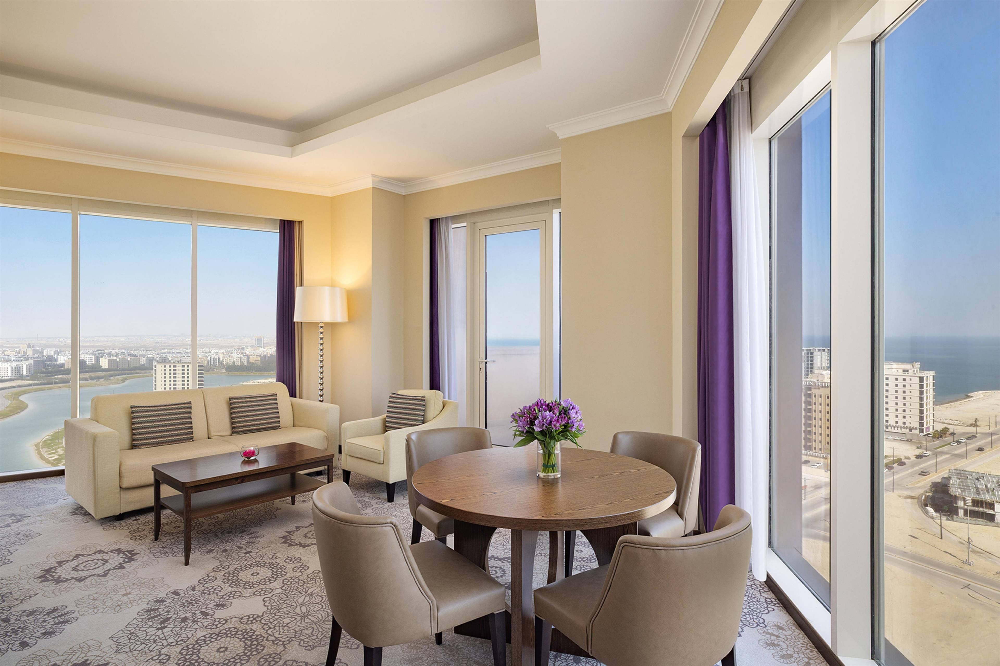 Habitación de hotel con un ventanal grande, un sofá, una mesa redonda y vistas de la ciudad.