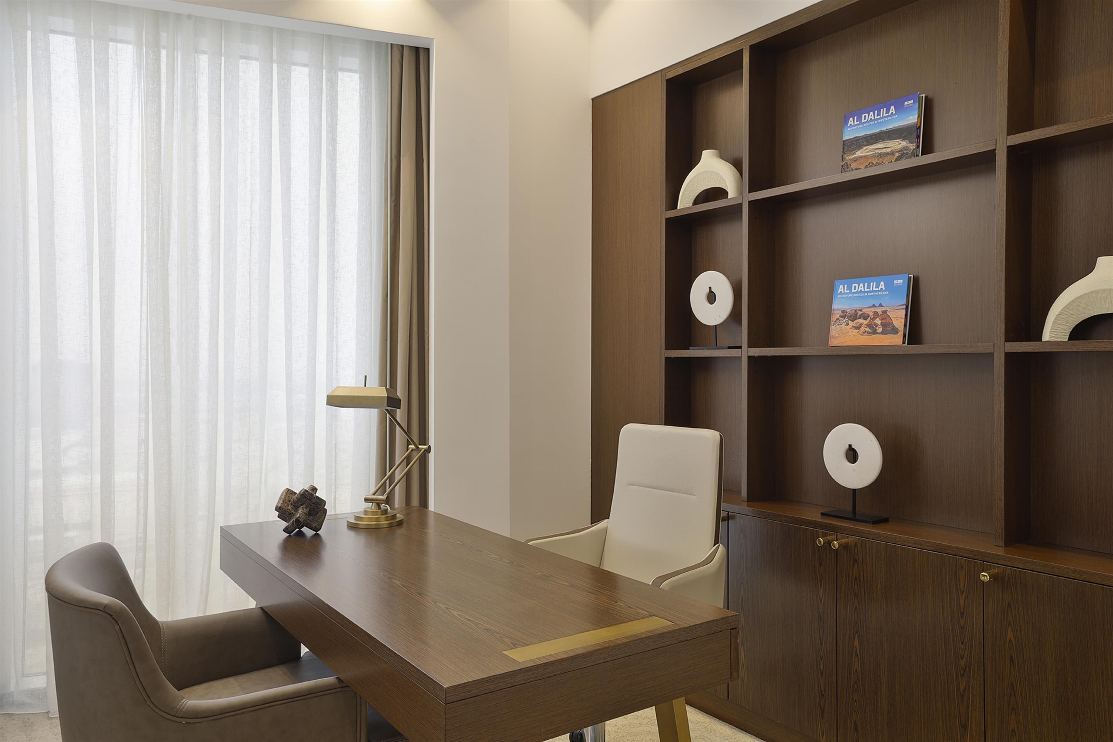 Un bureau moderne avec un bureau en bois, une chaise blanche et une bibliothèque contenant des livres et des objets décoratifs.