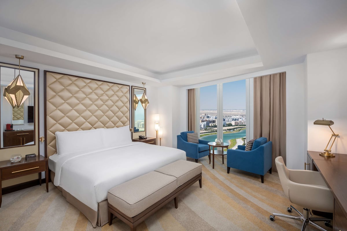 Quarto de hotel com uma cama grande, uma mesa, uma cadeira, um sofá e vista para a cidade.