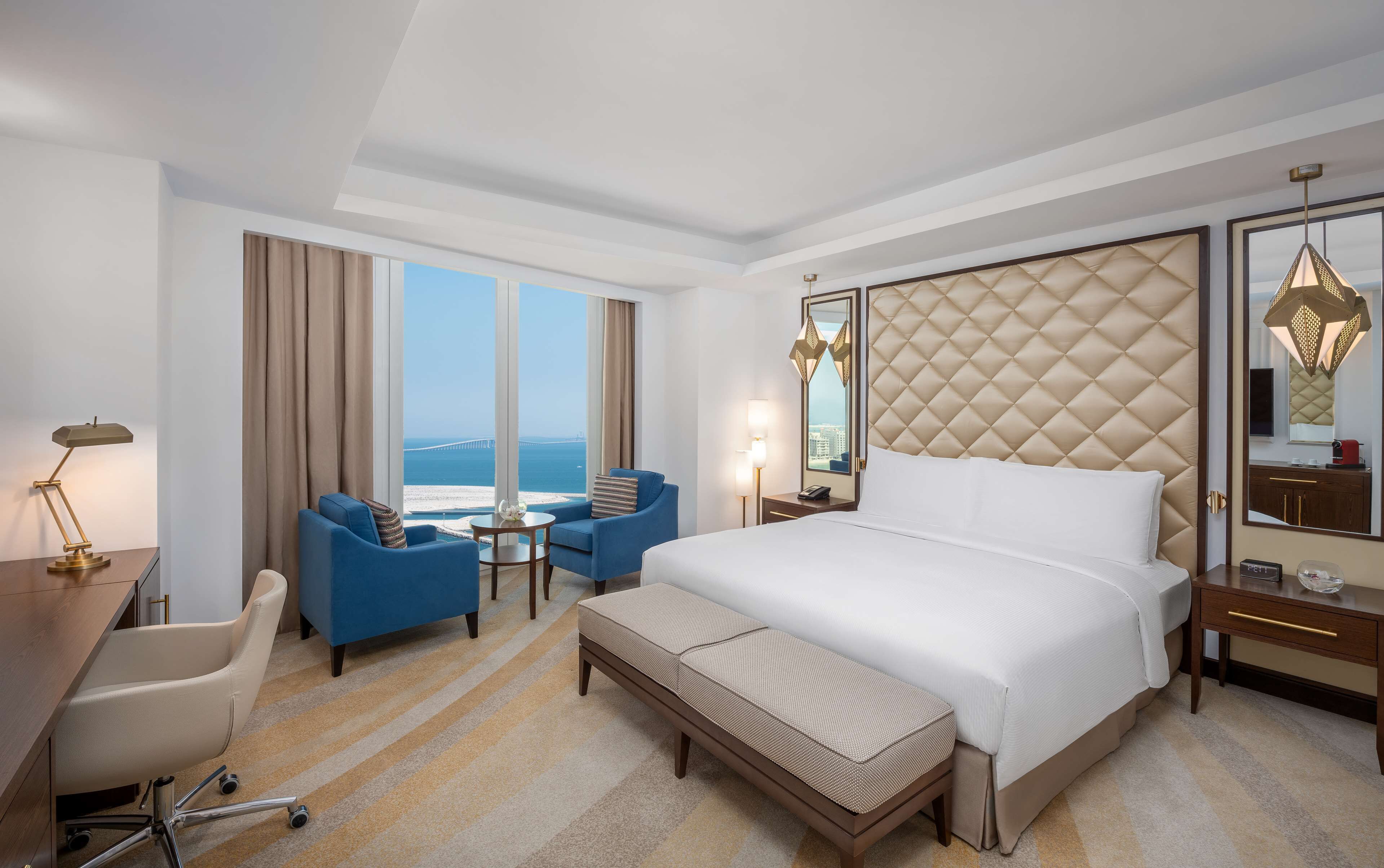 Une chambre d’hôtel avec un grand lit, un bureau, une chaise, une petite table et une vue sur la mer.