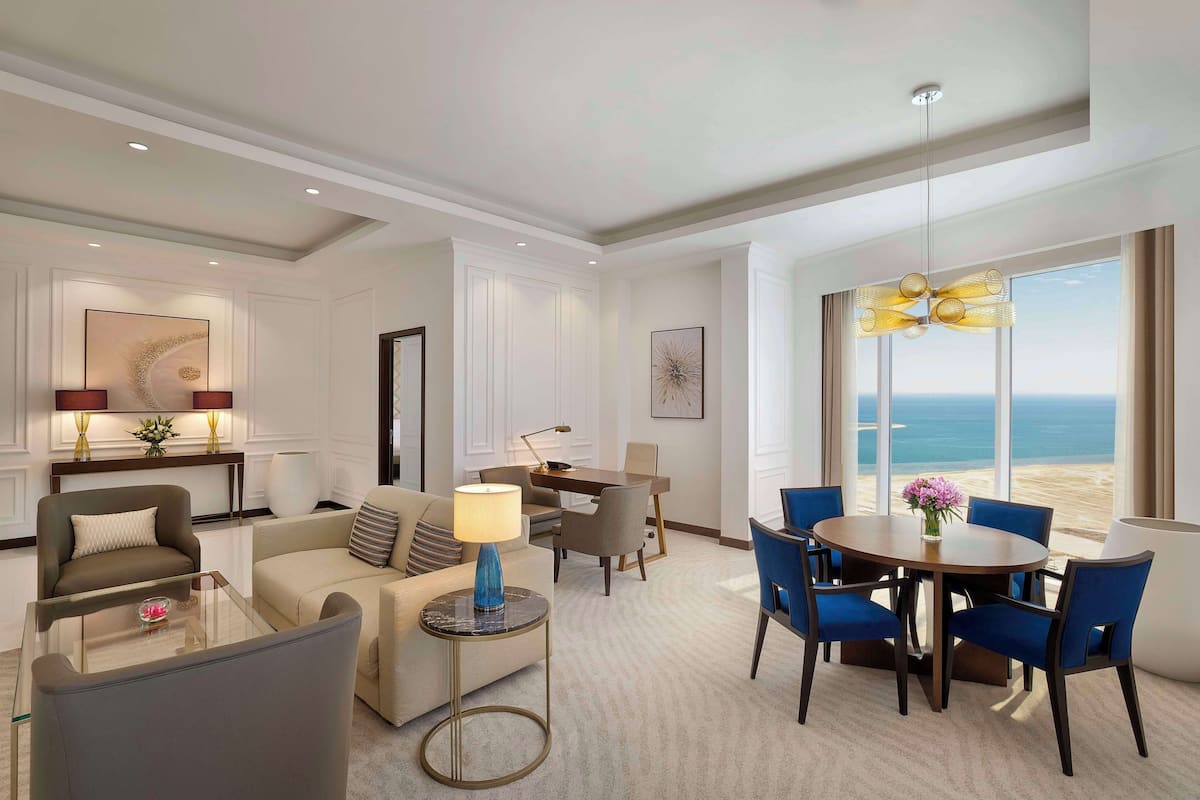 Quarto de hotel moderno com área de refeições, sofás e vista para o oceano.