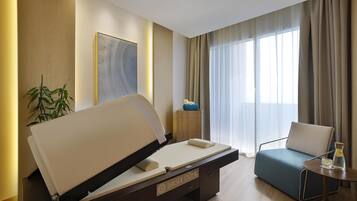 A modern hotel room with a bed, a sofa, a small table with a glass, and a plant.