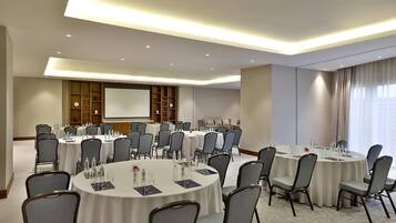 A conference room with multiple round tables, chairs, and a large screen for presentations.