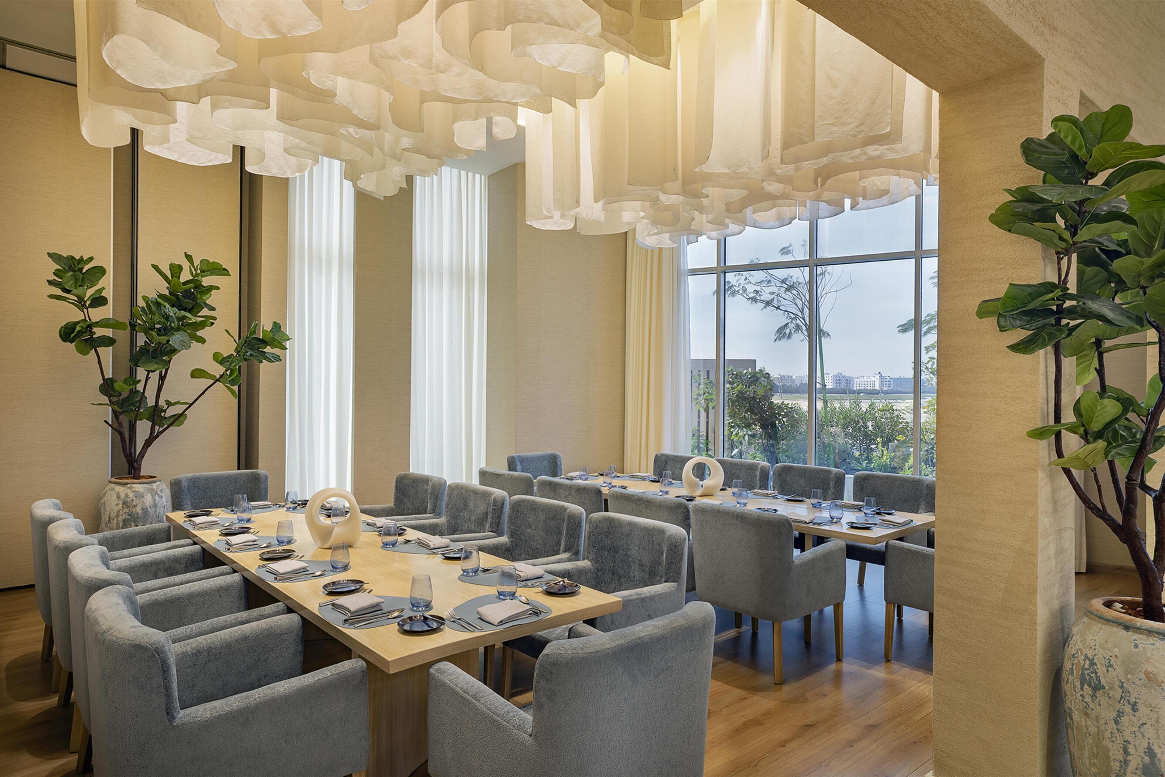 A conference room with a long table, multiple chairs, and large windows offering a view of the cityscape.