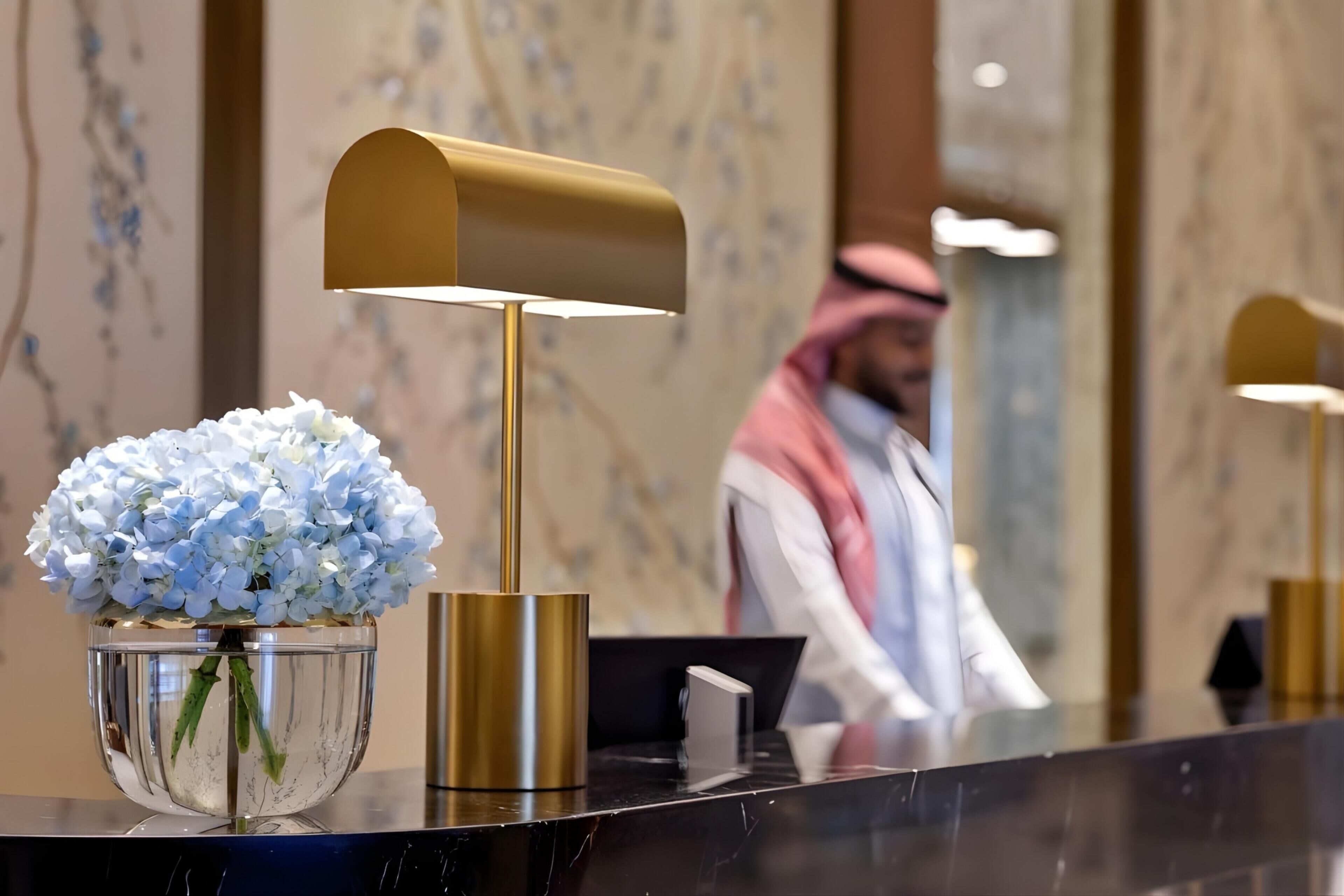 A reception desk with a gold mailbox, a glass vase with white flowers, and a marble wall in the background.